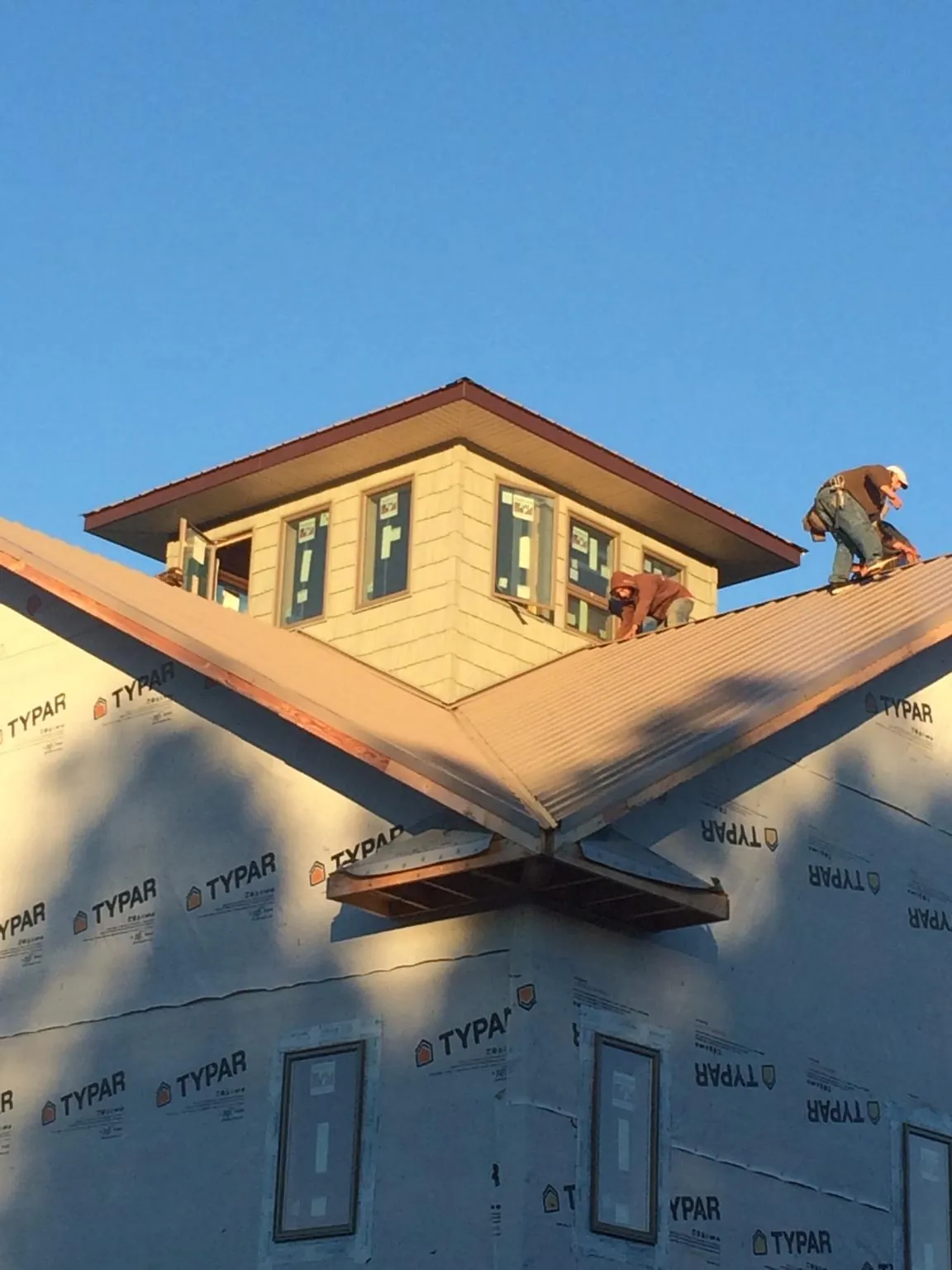Roofers working around a rooftop cupola on a new metal roof at sunset — Roof Waterproofing in Leonard by Roofing Brothers